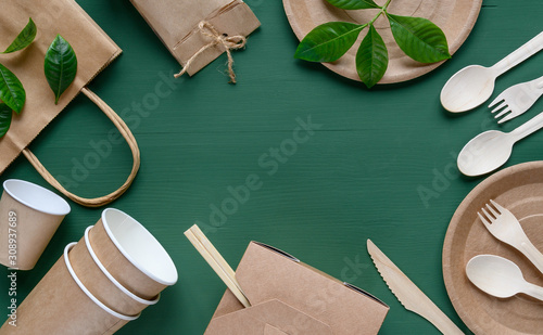 Recycled Eco-friendly disposable tableware made of paper on a green background. Wooden spoons, fork, knive, with paper cups, box, bamboo chopstic. photo