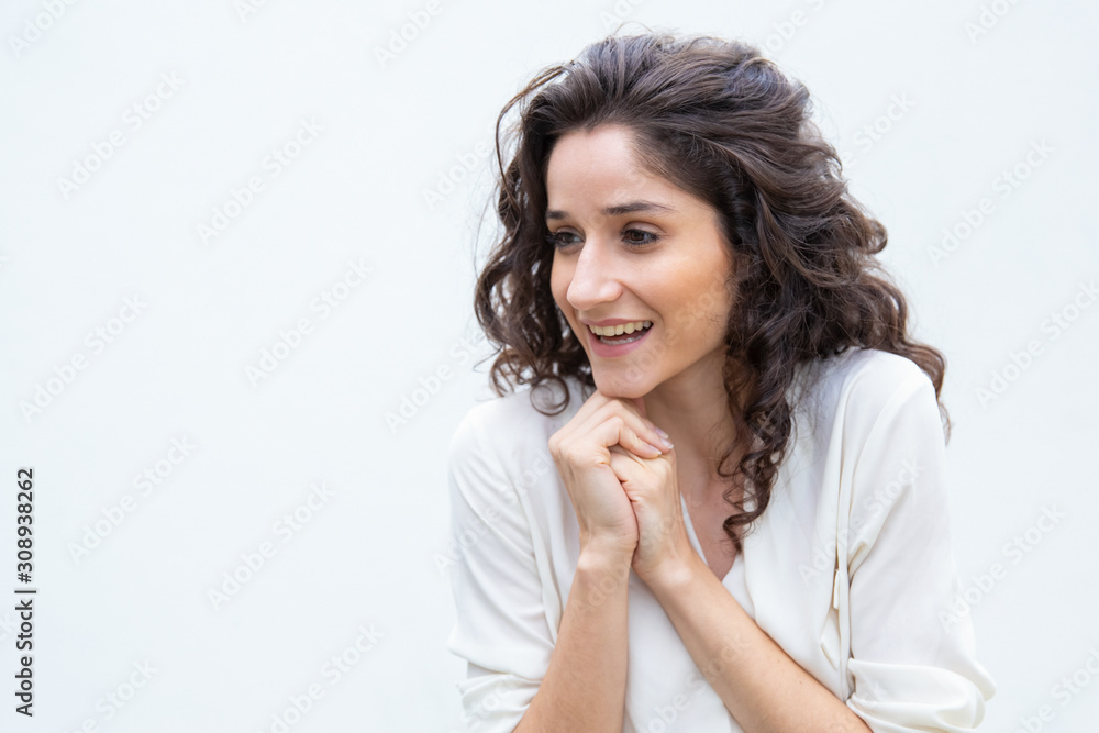 Happy joyful woman with clasped hands looking away. Wavy haired young woman in casual shirt standing isolated over white background. Positive emotions concept Happy joyful woman with clasped hands looking away. Wavy haired young woman in casual shirt standing isolated over white background. Positive emotions concept