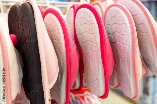 Several pairs of pink and beige Slippers with rubber soles hang on the counter in the store.