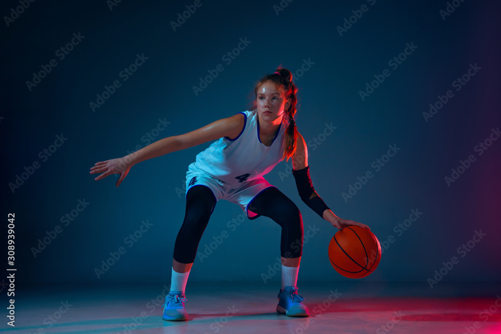 Movement. Young caucasian female basketball player on blue studio background in neon light, motion and action. Concept of sport, movement, energy and dynamic, healthy lifestyle. Training, practicing. Movement. Young caucasian female basketball player on blue studio background in neon light, motion and action. Concept of sport, movement, energy and dynamic, healthy lifestyle. Training, practicing.