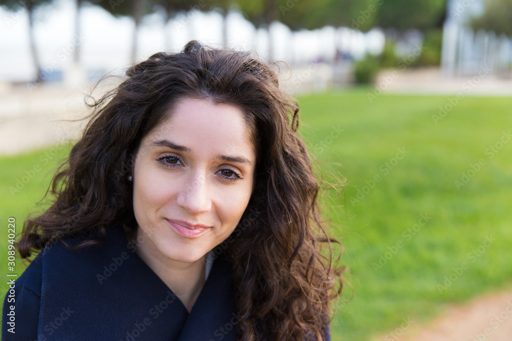 Closeup of happy cheerful beautiful student girl enjoying walking in park. Wavy haired young woman in casual overcoat posing outside. Outdoor female portrait or lifestyle concept Closeup of happy cheerful beautiful student girl enjoying walking in park. Wavy haired young woman in casual overcoat posing outside. Outdoor female portrait or lifestyle concept