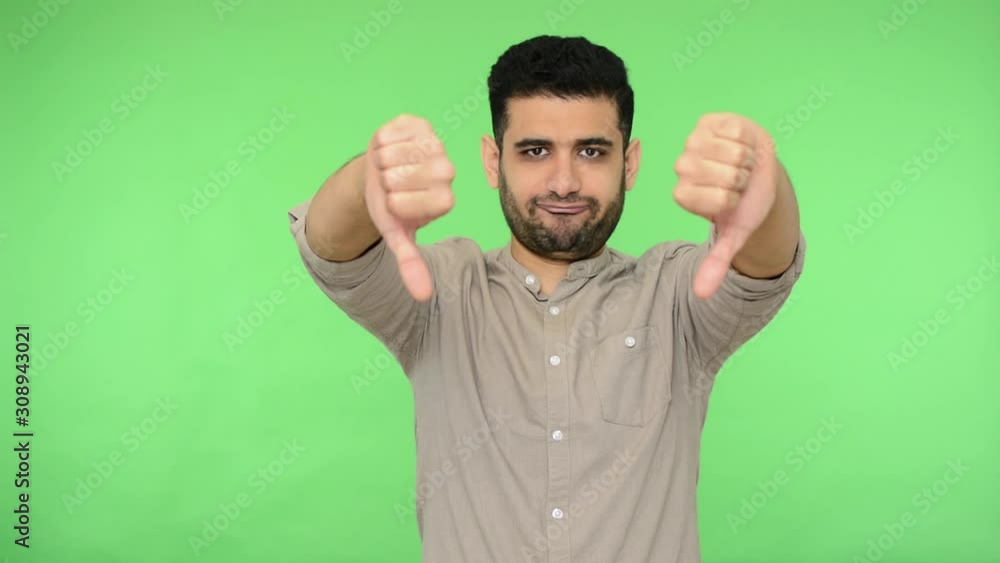 Dislike, negative feedback. Displeased brunette man with bristle in shirt showing double thumbs down gesture, denying offer with dissatisfied grimace. indoor studio shot, green background, chroma key Dislike, negative feedback. Displeased brunette man with bristle in shirt showing double thumbs down gesture, denying offer with dissatisfied grimace. indoor studio shot, green background, chroma key