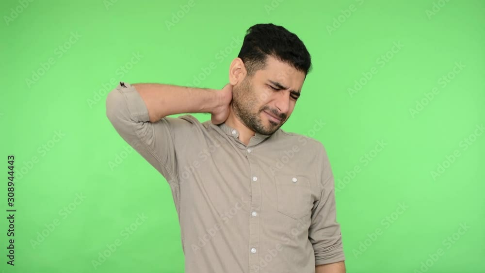 Neckache. Exhausted brunette man with bristle in shirt massaging neck and grimacing from pain, suffering backache, looking tired, overwork concept. indoor studio shot, green background, chroma key Neckache. Exhausted brunette man with bristle in shirt massaging neck and grimacing from pain, suffering backache, looking tired, overwork concept. indoor studio shot, green background, chroma key