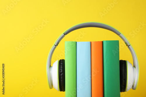 Books with modern headphones on yellow background. Space for text
