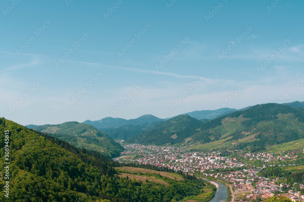 top view of landscape of river in valley and town under blue sky among high mountains covered with green wood