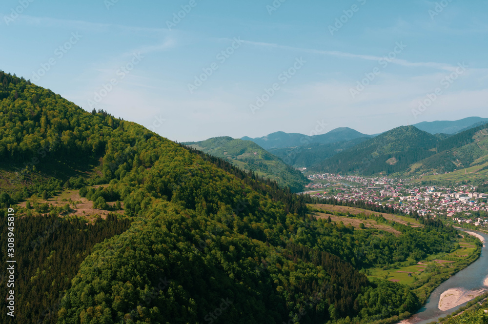top view of landscape of valley with river, town and sky among high mountains covered with green trees