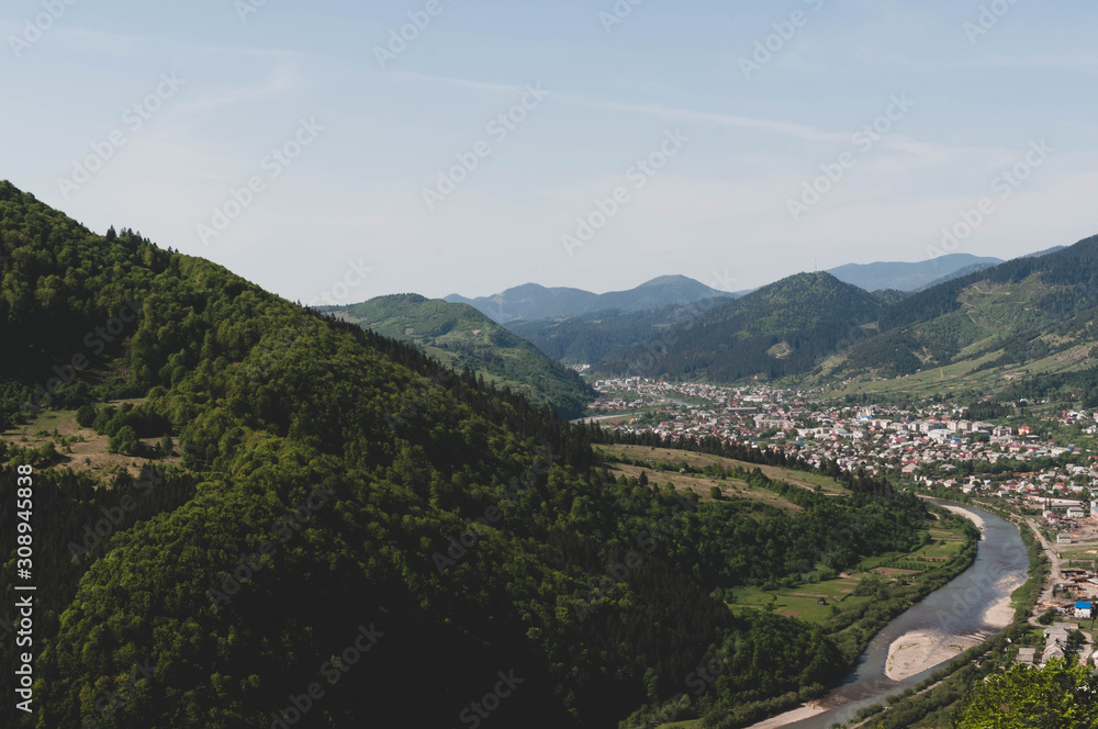 top view of valley with river and town and sky among mountains covered with green trees
