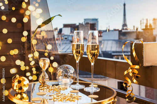 Celebration of New Year or Christmas concept. Two glasses with champagne and golden decorations on a balcony with a view on rooftops and Eiffel Tower.