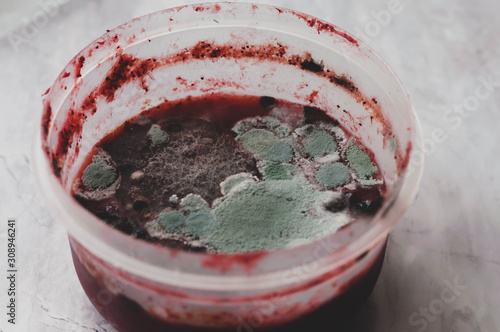 soft focus of spoiled red strawberry smoothie covered with toxic mold in plastik container on marble surface 
