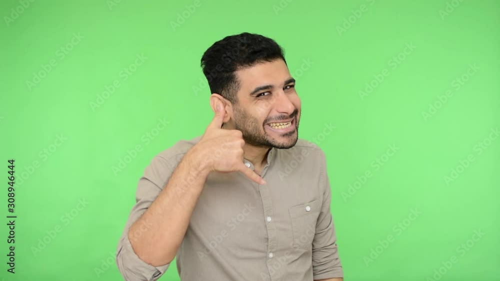 Handsome brunette man with bristle in shirt making phone gesture near head, saying hey you call me and pointing to camera, flirting with playful look. indoor studio shot, green background, chroma key Handsome brunette man with bristle in shirt making phone gesture near head, saying hey you call me and pointing to camera, flirting with playful look. indoor studio shot, green background, chroma key