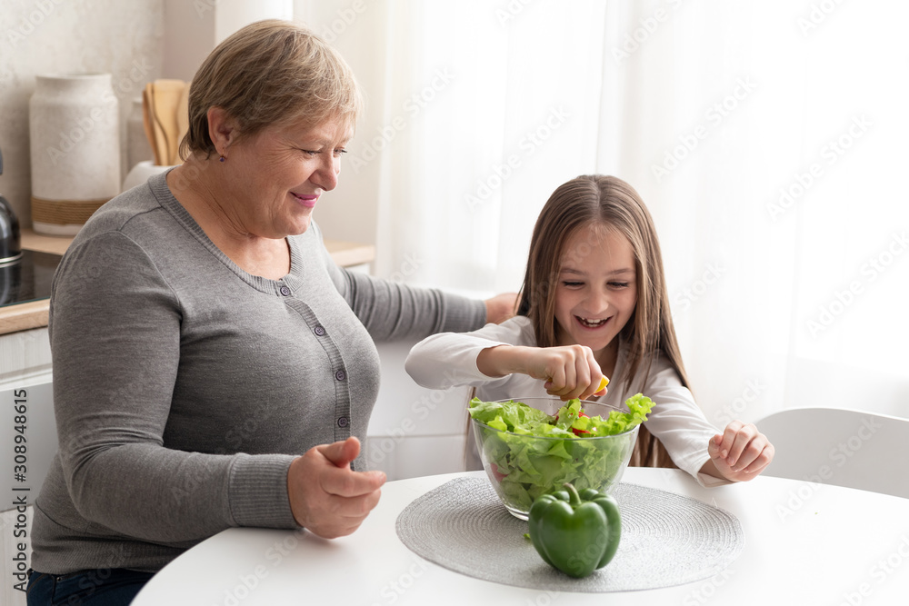 Grandmother and teen granddaughter prepare healthy food in the kitchen. Smiley family preparing a salad together Grandmother and teen granddaughter prepare healthy food in the kitchen. Smiley family preparing a salad together