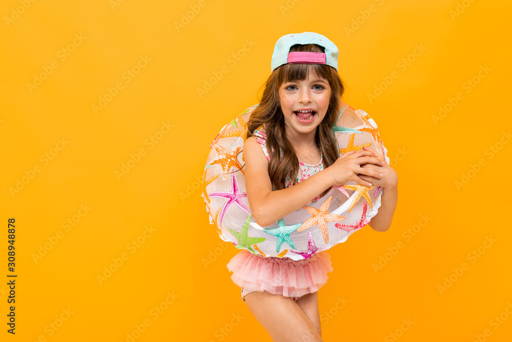 little european girl with a baseball cap in a swimsuit with a swimming circle on a yellow background little european girl with a baseball cap in a swimsuit with a swimming circle on a yellow background