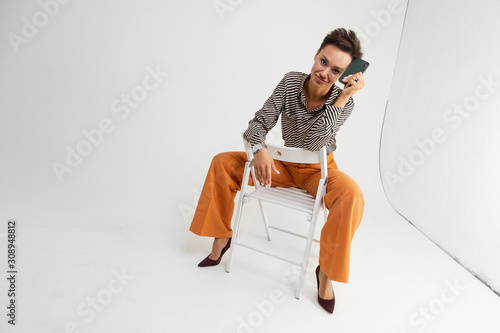 elegant lady with a short haircut in classic pants and a shirt posing sitting on a chair on a white background
