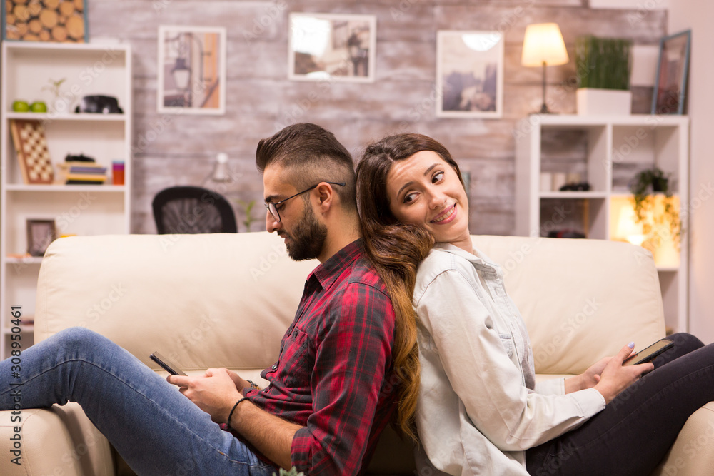 Girlfriend looking at her boyfriend while sitting back to back Girlfriend looking at her boyfriend while sitting back to back