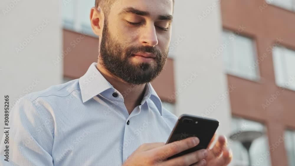 Close up view of Happy bearded businessman using smartphone while sitting outdoors Close up view of Happy bearded businessman using smartphone while sitting outdoors