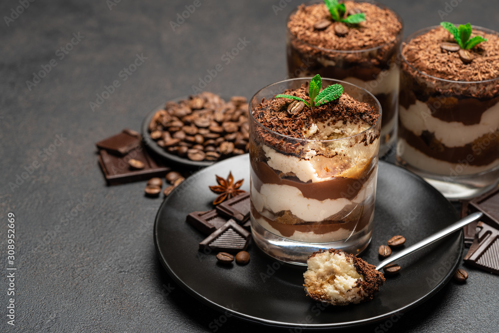 Classic tiramisu dessert in a glass cup and pieces of chocolate on dark concrete background Classic tiramisu dessert in a glass cup and pieces of chocolate on dark concrete background