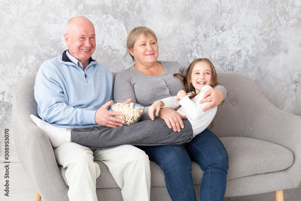 Grandparents together with granddaughter watching tv, movie indoors