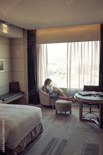  Woman relaxing in the armchair near the window in a hotel room