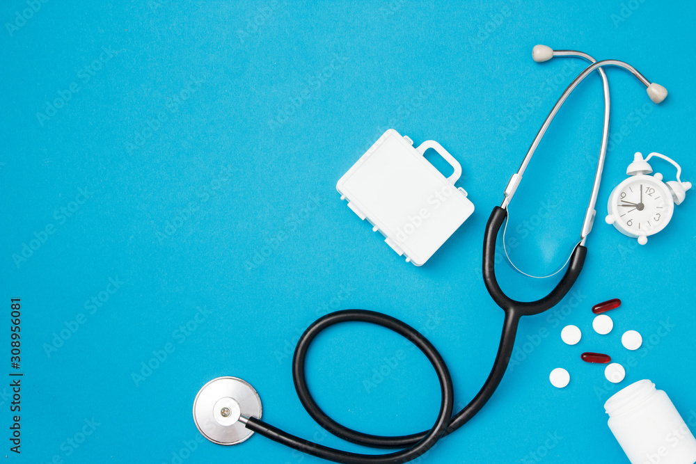 Stethoscope with pills and alarm clock on blue background. Health care and medical examination concept. Top view, flat lay, copy space. - obrazy, fototapety, plakaty 