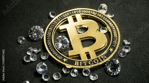 Shiny gold bitcoin virtual currency coin laying on black table with diamonds