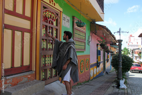 Man with poncho knocking on the door of his colorful house © Frenchiebuddha