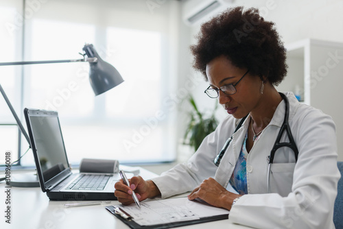 Serious concentrated African American doctor working in her office at clinic photo