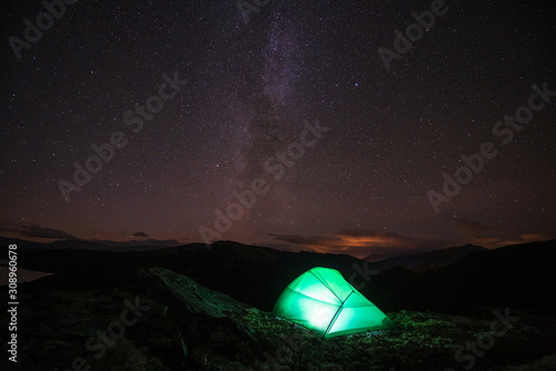Milky way and starry sky over night scene outdoors in the forest and the mountains with green tent infront. Landscape  astronomy and camping concept.