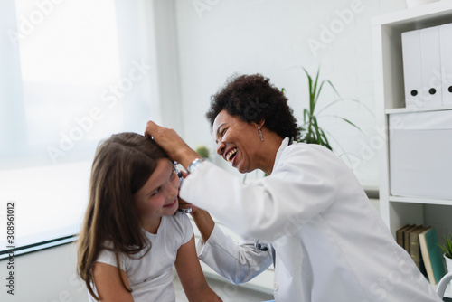 Woman afro american doctor general practitioner examining ear of a ill child. Ear infections. photo