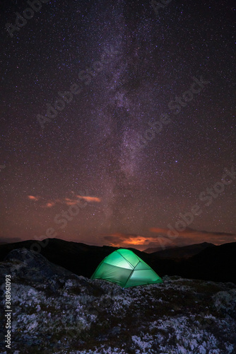 Milky way and starry sky over night scene outdoors in the forest and the mountains with green tent infront. Landscape, astronomy and camping concept. Vertical shot.