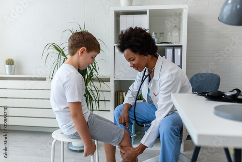 Woman African American doctor general practitioner examining child's patellar knee-jerk reflex photo