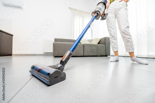Woman cleaning floor with cordless vacuum cleaner in the modern white living room. Concept of easy cleaning with a wireless vacuum cleaner