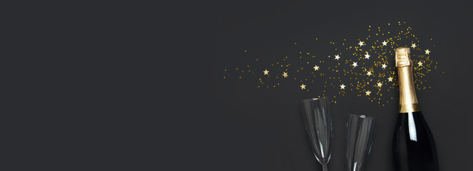 Christmas and New Year background. Champagne bottle, champagne glasses, festive golden star confetti on black background top view. Flat lay holiday card. Birthday or party concept. Festive decorations