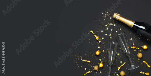 Christmas and New Year background. Champagne bottle champagne glasses golden christmas balls festive ribbons star confetti on black background top view. Flat lay holiday card. Party decorations 2020