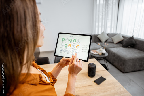 Young woman controlling home with a digital touch screen panel. Concept of a smart home and mobile application for managing smart devices at home