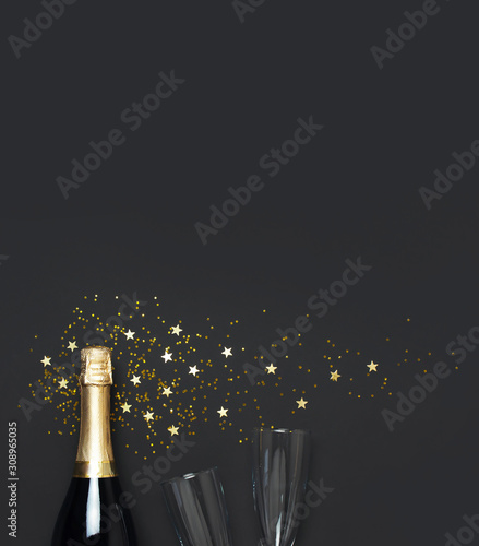Christmas and New Year background. Champagne bottle, champagne glasses, festive golden star confetti on black background top view. Flat lay holiday card. Birthday or party concept. Festive decorations