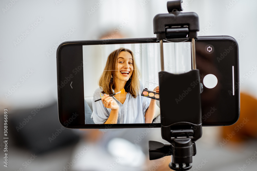 Young woman recording on a smart phone her vlog about cosmetics, showing and demonstrating makeup, close-up on phone. Influencer marketing in social media concept
