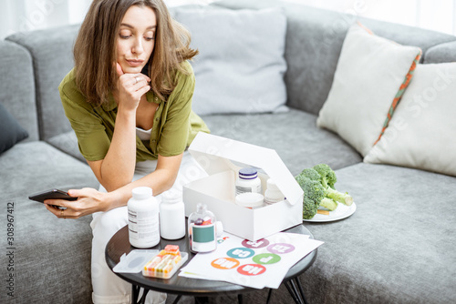 Quadro em tela Thoughtful woman with nutritional supplements at home