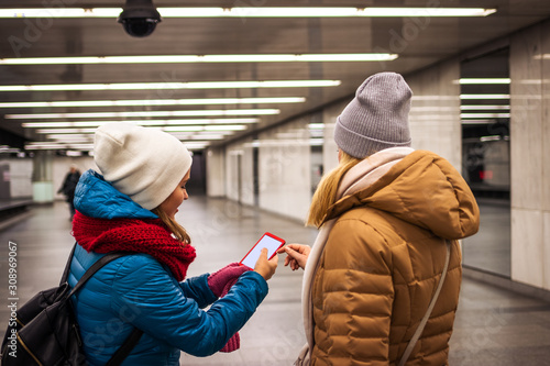 Two women buying ticket to subway by using mobile app. Young tourists using smart phone in subway station