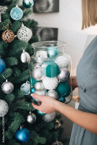 Young female woman holding a big decorating glass jar near the christmas tree with blue and white balls. Winter holidays and people concept