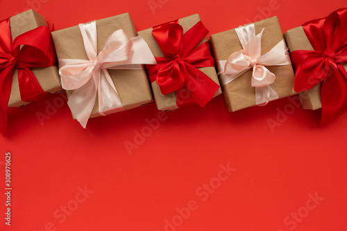Border from gift boxes wrapped brown craft paper and red and pink ribbon on red background. Valentines day or Christmas celebration concept. Top view