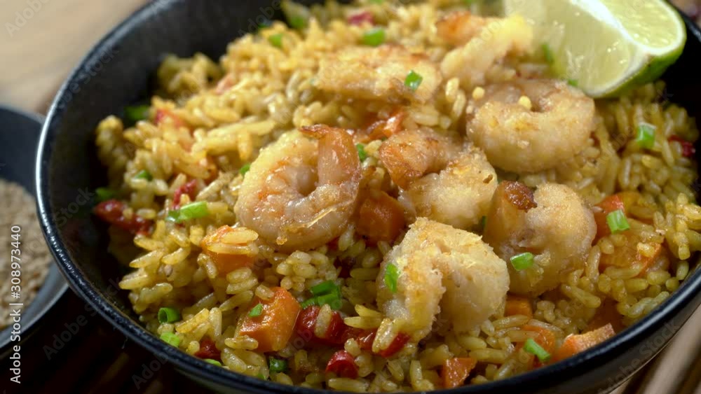 Traditional shrimps stir fried with eggs, vegetables and rice in a black bowl on a bamboo placemat. Healthy Asian meal with sesame and lime. Camera dolly and panning close-up follow focus shot. Traditional shrimps stir fried with eggs, vegetables and rice in a black bowl on a bamboo placemat. Healthy Asian meal with sesame and lime. Camera dolly and panning close-up follow focus shot.