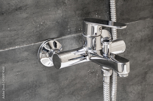 Chrome metal faucet for hot and cold water, with a shower hose, mounted in a wall covered with gray tile imitating concrete with water drops in a modern bathroom photo