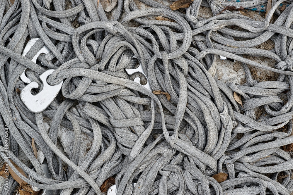 Tangled mess of gray guy lines with metal tensioners attached. Old and worn out, knotted and discarded on the ground. Used for tent camping and also securing loads on trucks.