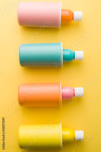 Bottle full of painting colors inside slim mug of different colors, attract composition on yellow background