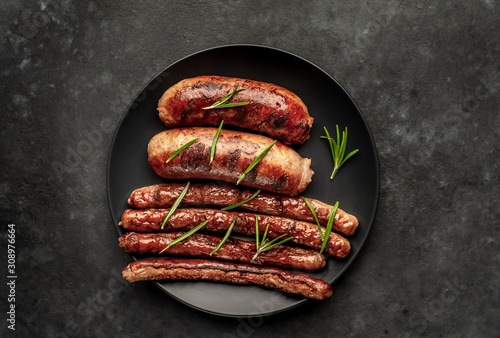 different grilled sausages in a dark plate with spices and rosemary, on a stone table, ready to eat with copy space for your text