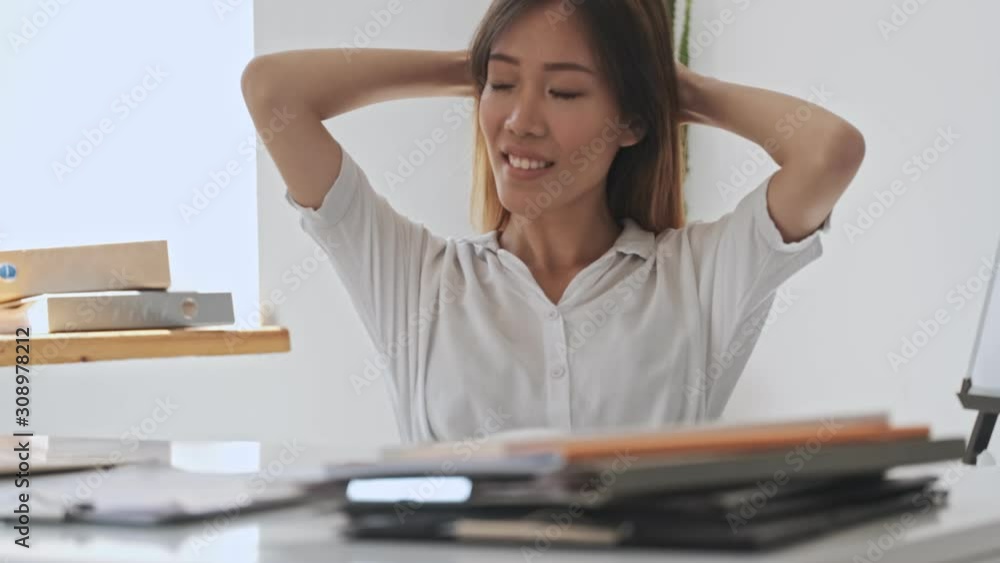 Happy dreaming asian business woman is looking to the side while sitting by the table in the office Happy dreaming asian business woman is looking to the side while sitting by the table in the office