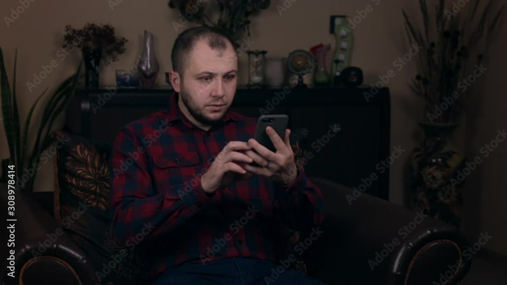 Shocked men reading message via smartphone. Upset young boy holding cell phone at home. Bad news concept Shocked men reading message via smartphone. Upset young boy holding cell phone at home. Bad news concept