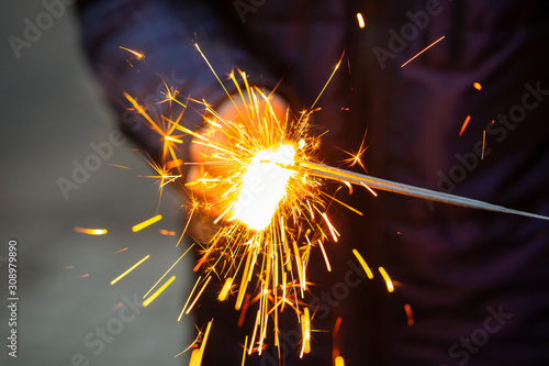Group of happy people holding sparklers at party. Guy holds in his hands lit sparklers. People celebrating New Year together. Friends lit sparklers. New Year and Christmas concept