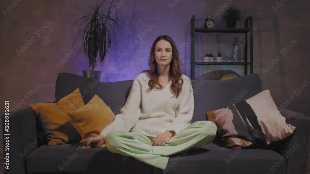 A young woman is sitting on a sofa in a cozy room watching TV. The girl is dissatisfied with what she sees on TV A young woman is sitting on a sofa in a cozy room watching TV. The girl is dissatisfied with what she sees on TV