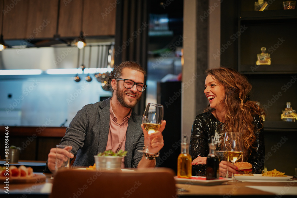 Attractive caucasian couple in love sitting in restaurant, drinking wine, smiling and flirting.